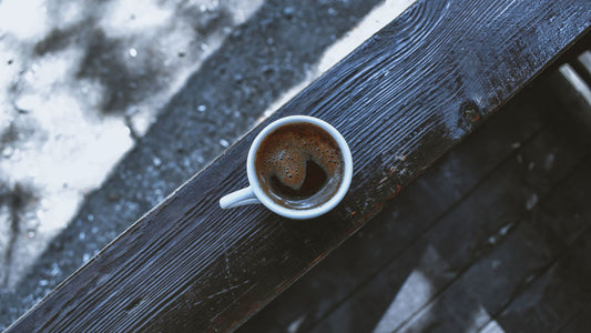 A mug of black coffee on a wooden table beside a notebook