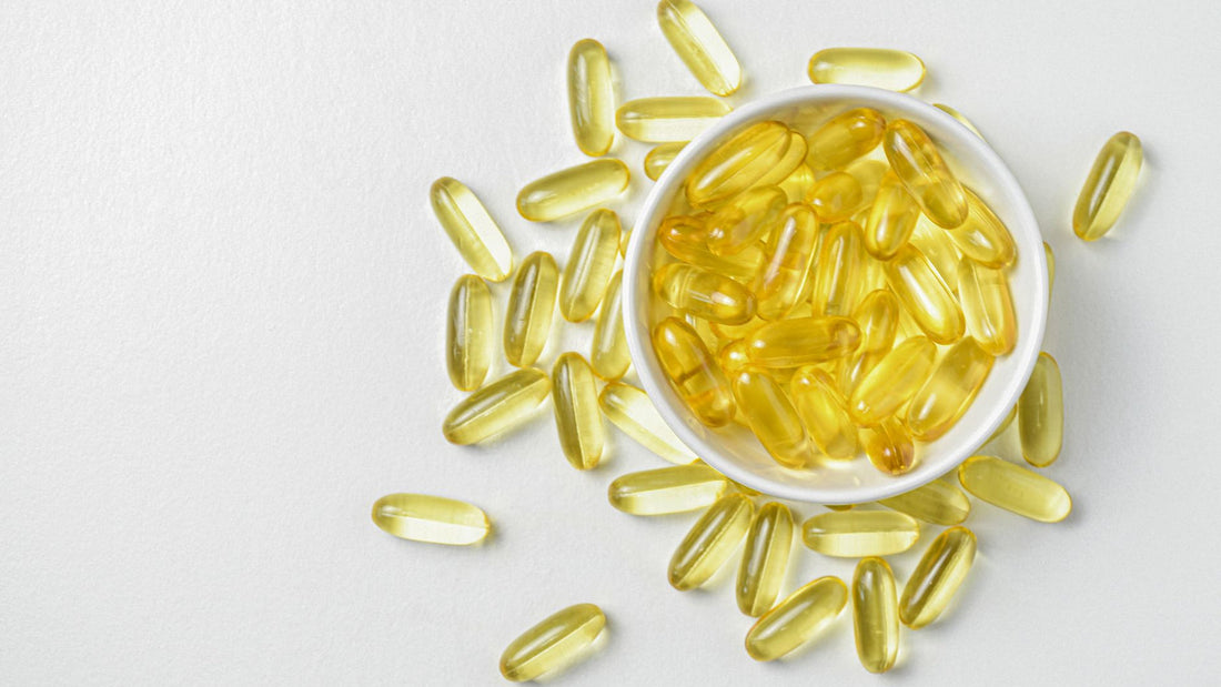 Amber softgel capsules in a small dish beside a glass of water on a kitchen counter