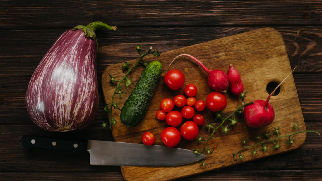 Fresh vegetables and fruit arranged on a wooden cutting board in a kitchen