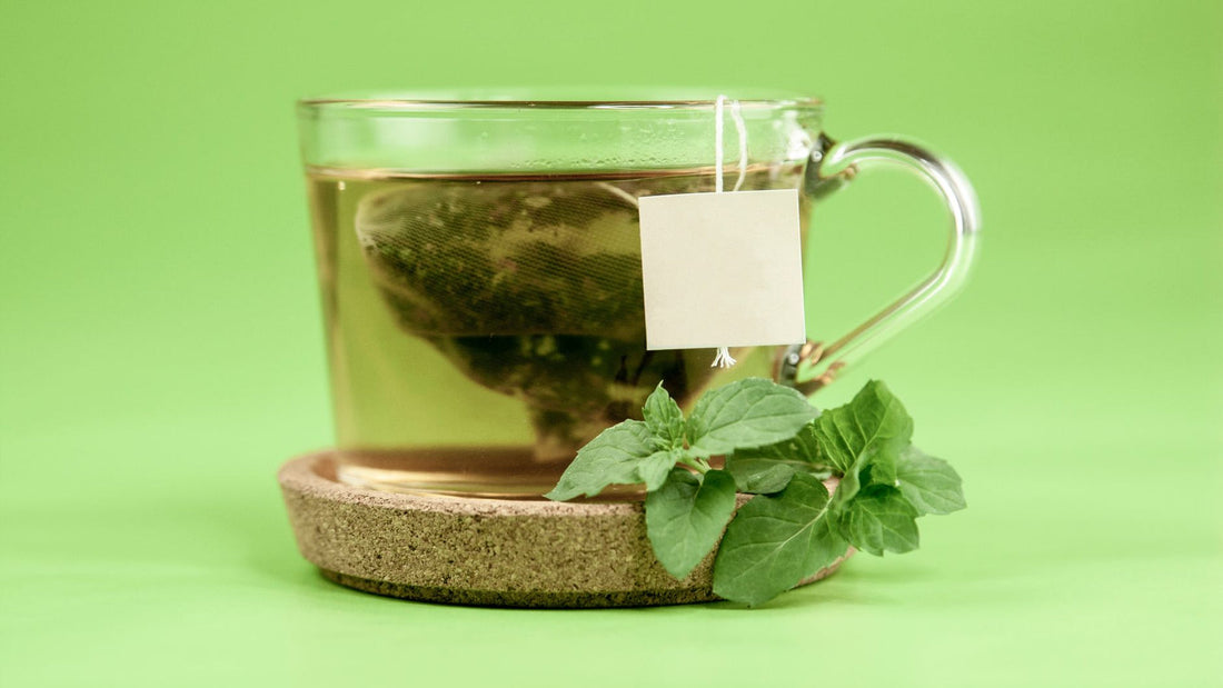 Cup of brewed green tea beside loose tea leaves on a wooden table